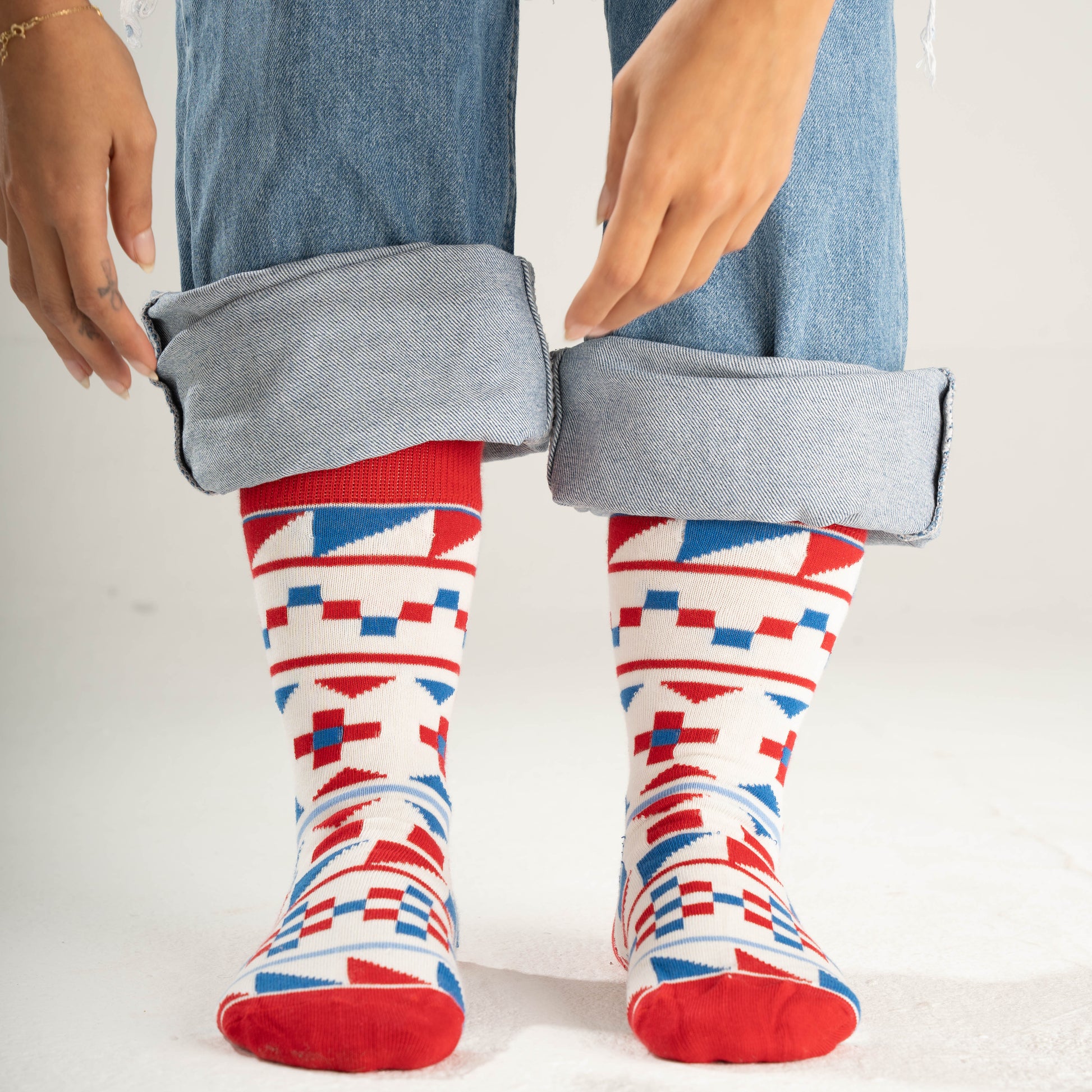 Person wearing colorful geometric-patterned socks with rolled-up jeans on a white background